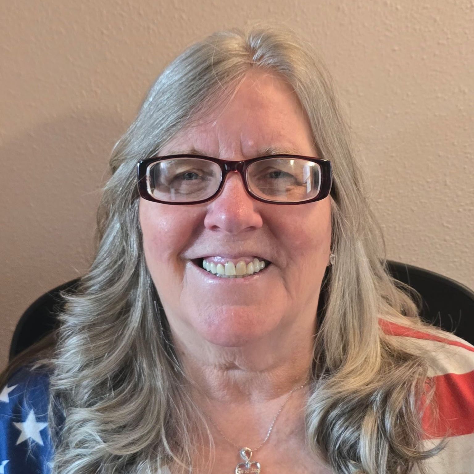 A woman wearing glasses and an american flag shirt is smiling.