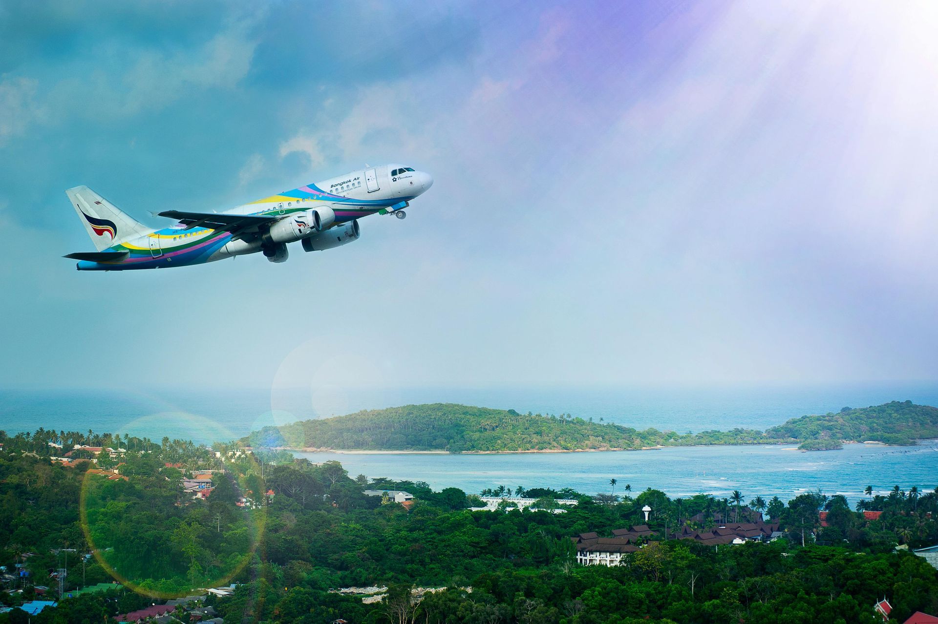 An airplane taking off over a tropical landscape with green hills, ocean, and a bright sky.