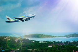An airplane taking off over a tropical landscape with green hills, ocean, and a bright sky.