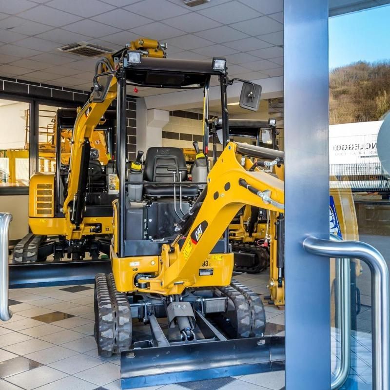 Miniescavatori gialli esposti all'interno di uno showroom, visibili attraverso una porta aperta.