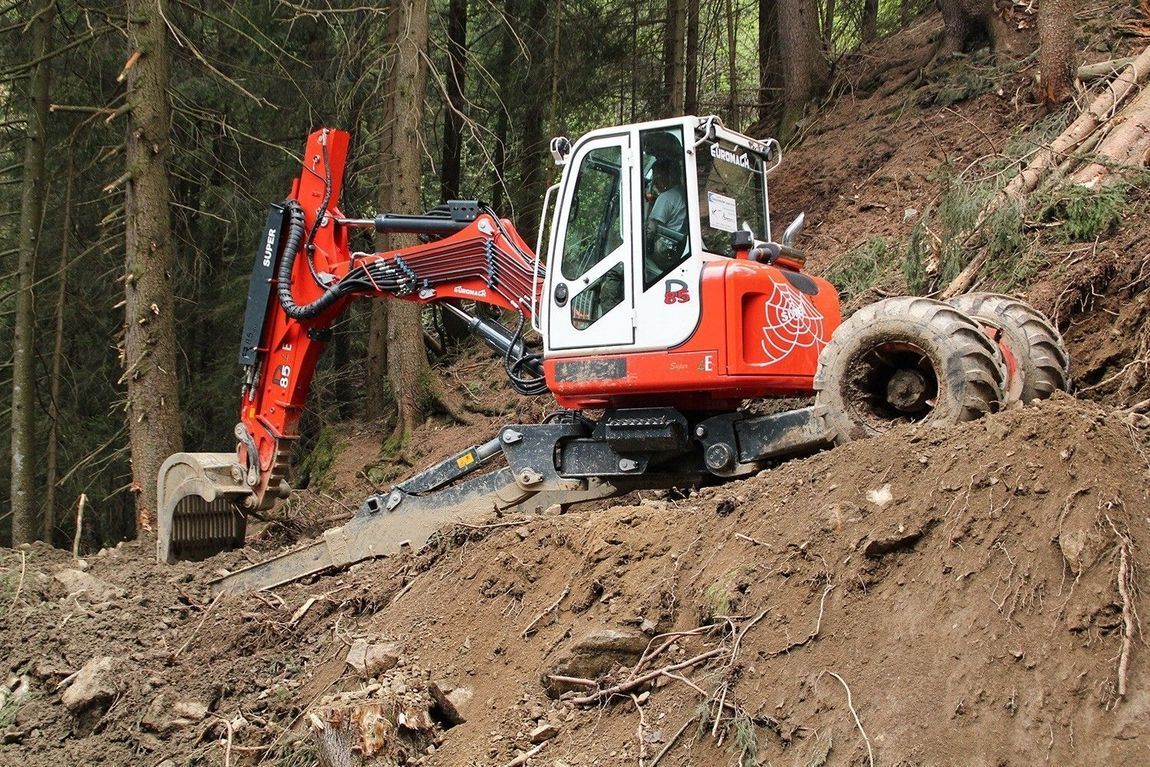 Escavatore arancione che scava nel pendio di una collina in una foresta.