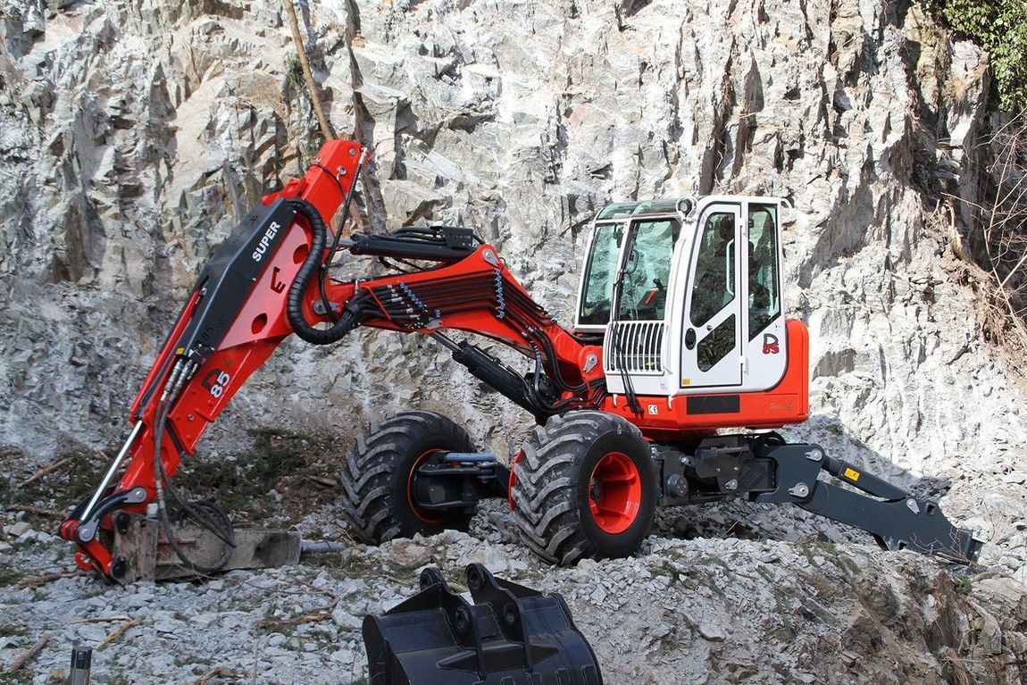 Escavatore gommato arancione e bianco che scava in un pendio roccioso.