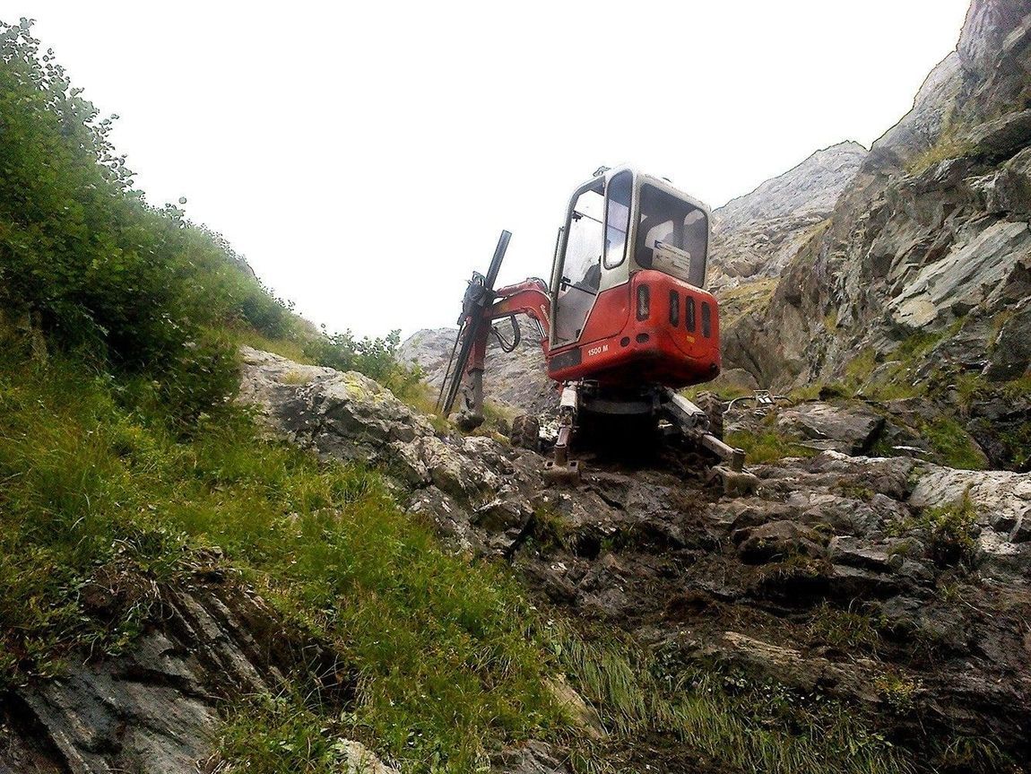 Escavatore rosso al lavoro su un pendio roccioso.