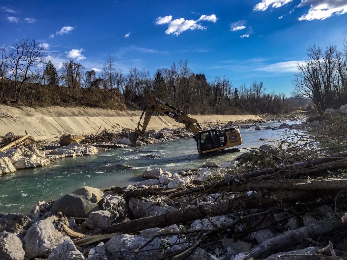 Escavatore nel fiume, che rimuove i detriti sotto un cielo azzurro.