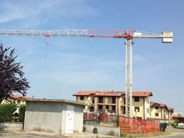 Gru da costruzione davanti a diverse case incompiute, sotto un cielo azzurro.