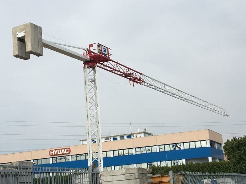 Gru da costruzione con contrappeso in cemento armato che si estende sopra un edificio. Struttura metallica rossa e bianca.