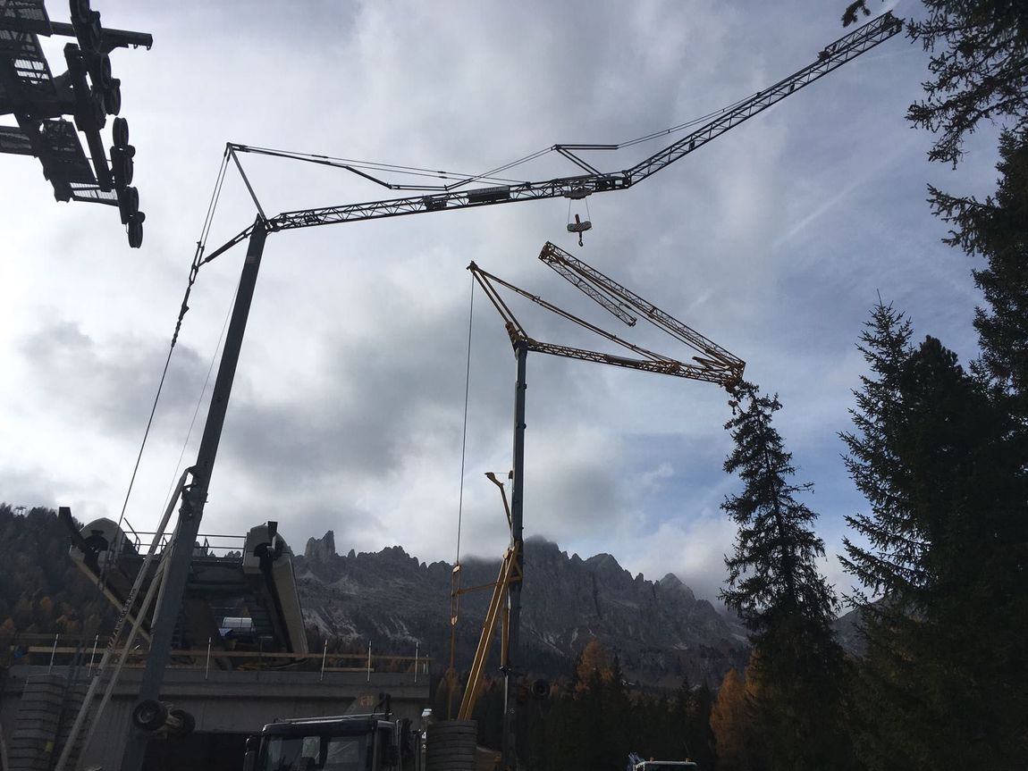 Diverse gru in funzione in un cantiere edile con sfondo montuoso e cielo nuvoloso.