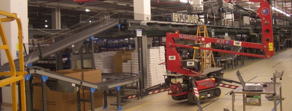 Interno di un magazzino con un nastro trasportatore e un carrello elevatore rosso.