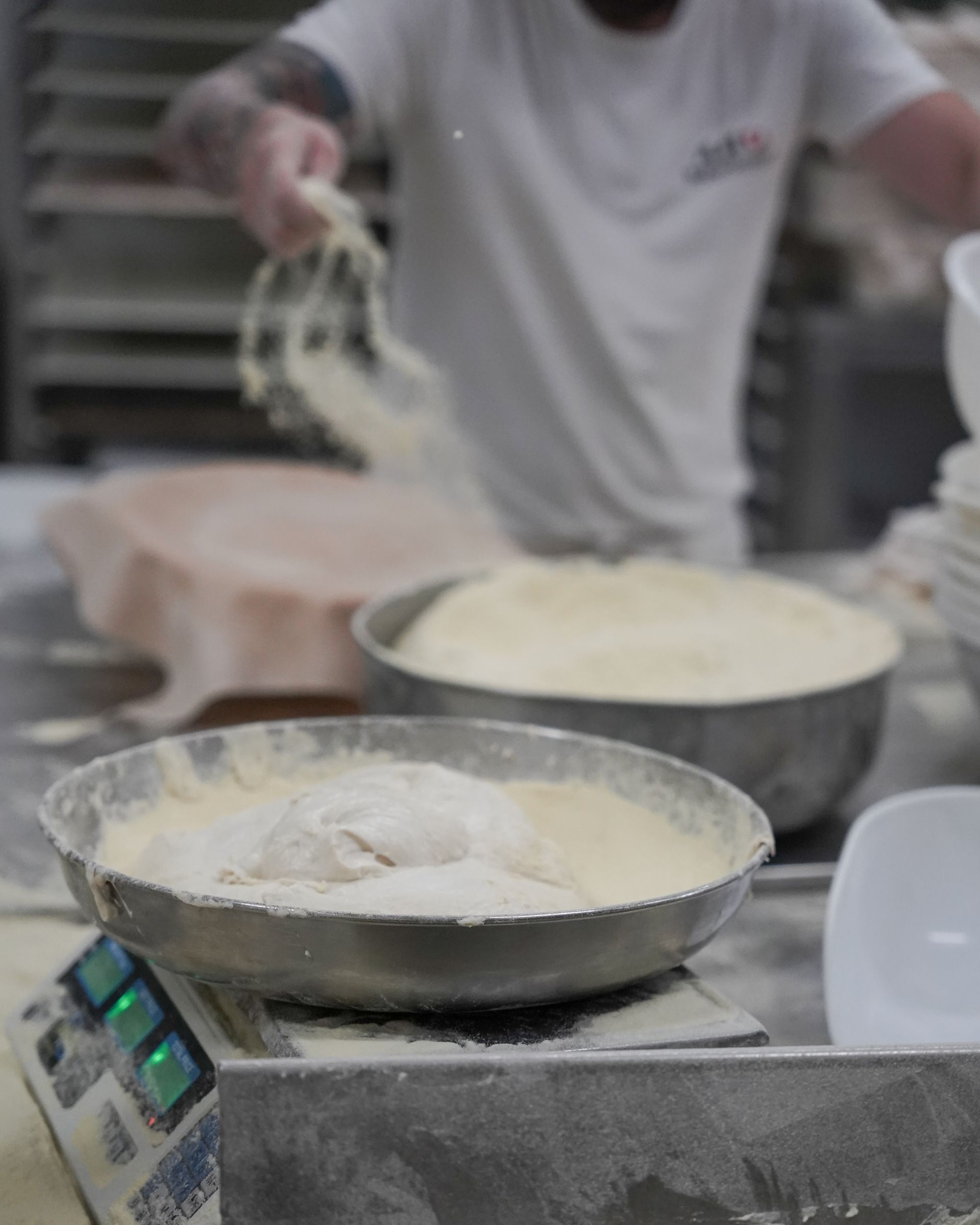 Un fornaio aggiunge la farina all'impasto in ciotole di acciaio inossidabile su una bilancia in un panificio.