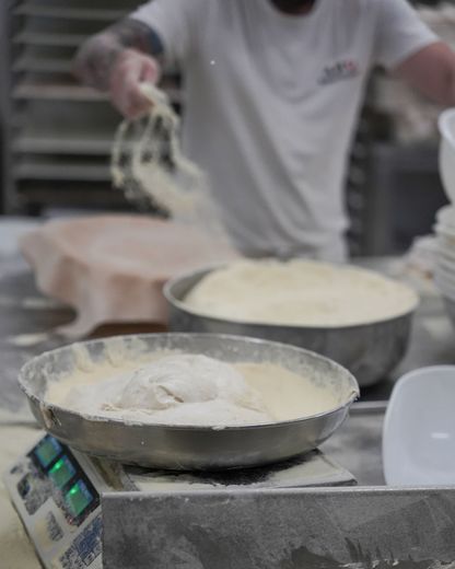 Un fornaio aggiunge la farina all'impasto in ciotole di acciaio inossidabile su una bilancia in un panificio.