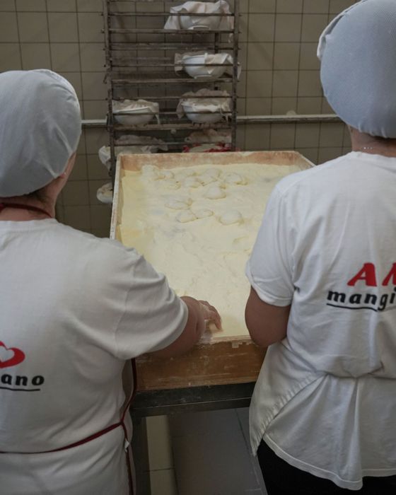 Due persone con camicie bianche e retine per capelli preparano il cibo in cucina.