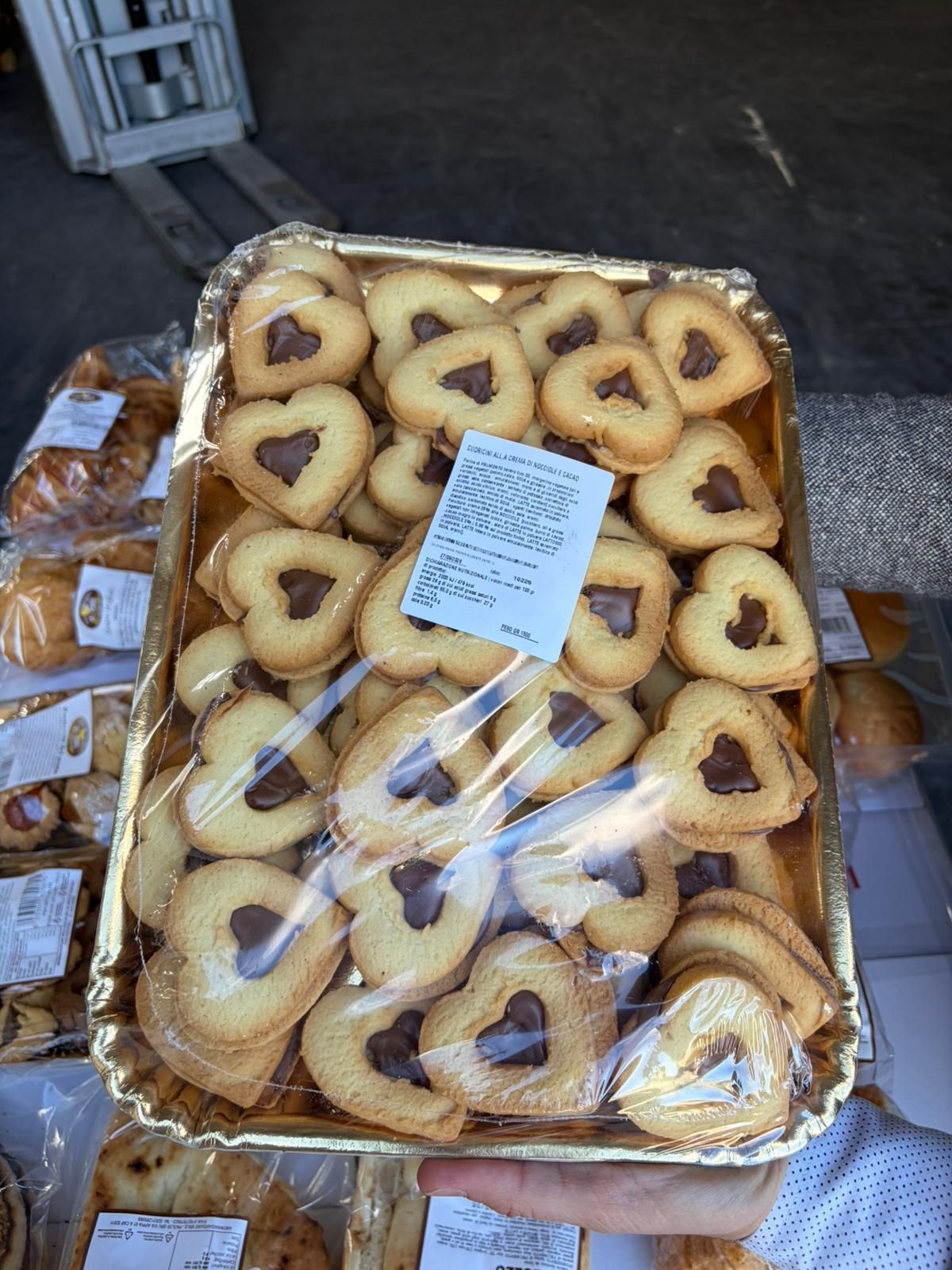 Vassoio di biscotti a forma di cuore con cuore di cioccolato, avvolti nella pellicola. Sostenuto da una persona all'aperto.