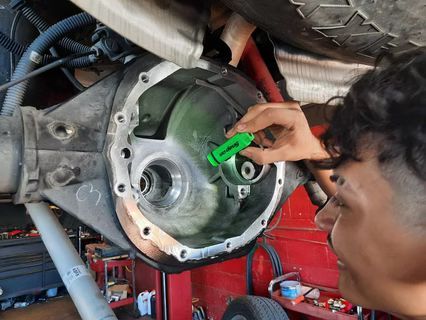 Person examining a vehicle's open differential, pointing with a green tool, likely at internal components. | Lains Auto Service