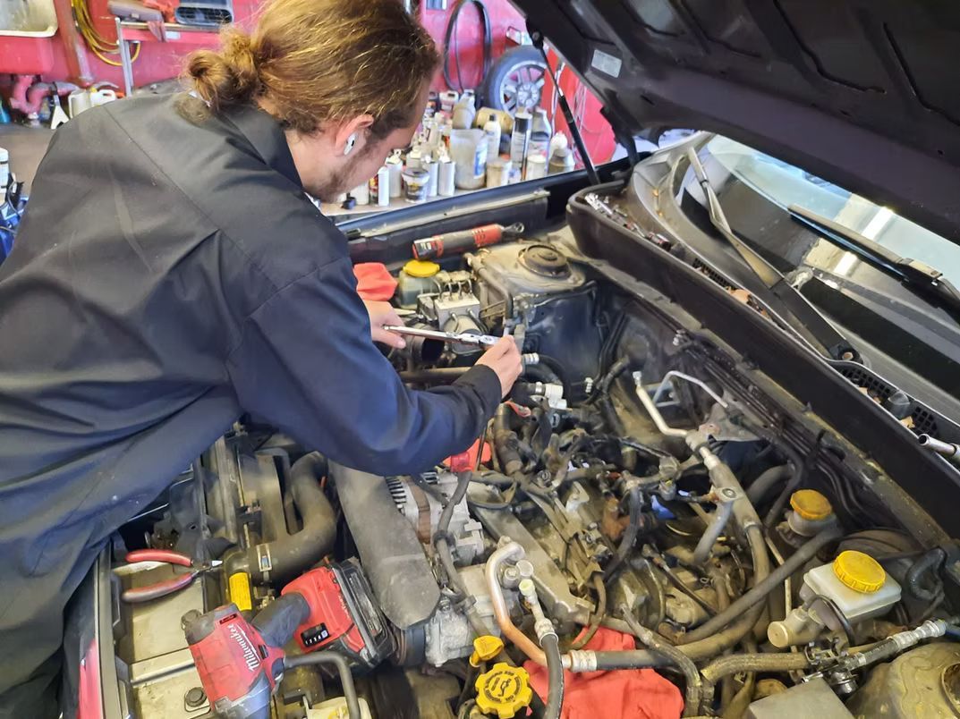Mechanic working on a car engine under the open hood in a garage. | Lains Auto Service