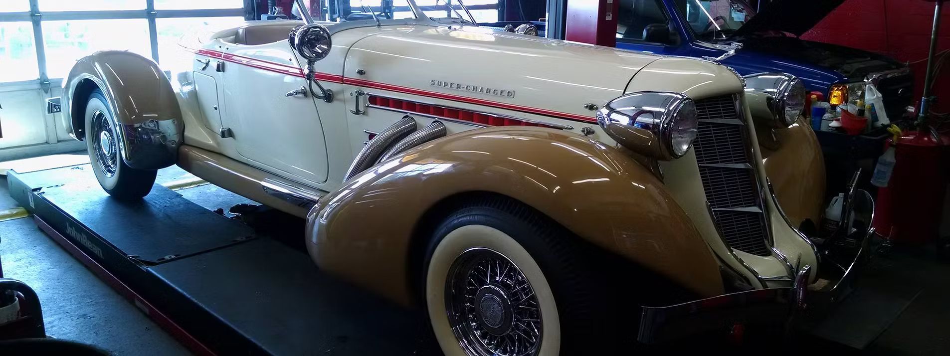 A vintage cream and tan Auburn Speedster roadster on a repair lift. | Lains Auto Service