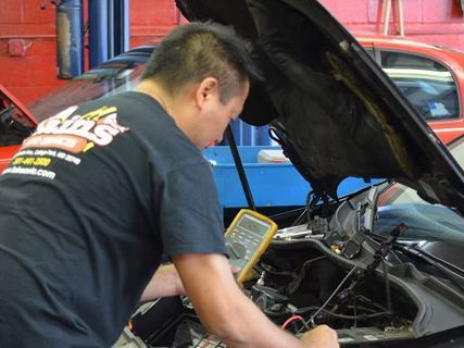 Mechanic working on a car engine in a garage; uses a multimeter. | Lains Auto Service