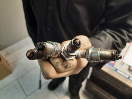 Hand holding four used, black-tipped spark plugs. | Lains Auto Service