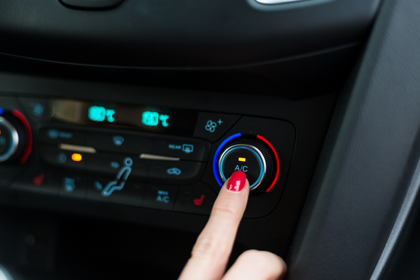 A hand with red nail polish presses the air conditioning button on a car's dashboard. | Lains Auto Services