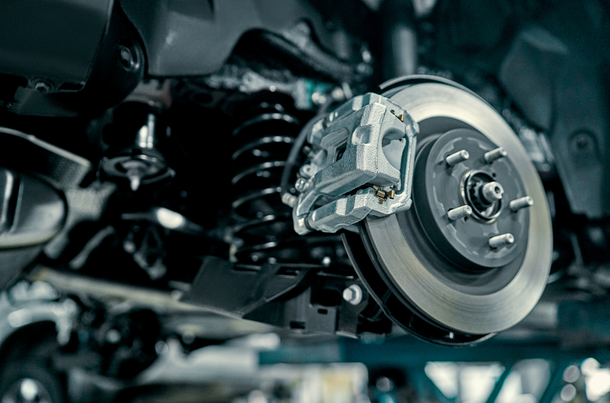 Car's brake system with disc rotor, caliper, and suspension components, shown from below with a close-up view. | Lains Auto Services