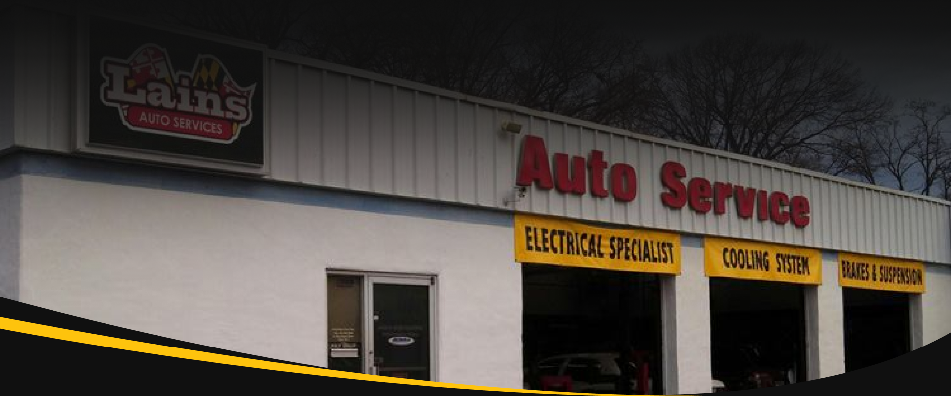 An auto service shop with a vehicle inside. The shop has an open bay door. | Lains Auto Services