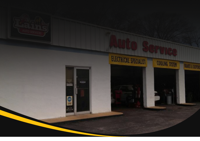 Exterior of an auto service shop with a car inside the bay. White building, red signage. | Lains Auto Services