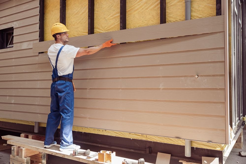 Construction worker in blue overalls installs siding on a building's exterior.