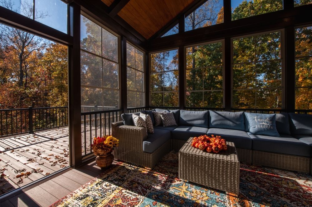 Screened porch with blue sectional, rug, and autumn foliage visible through windows.