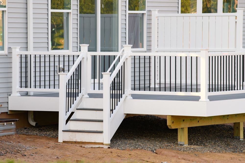 White deck with black railings and steps leading to a house with gray siding and windows.
