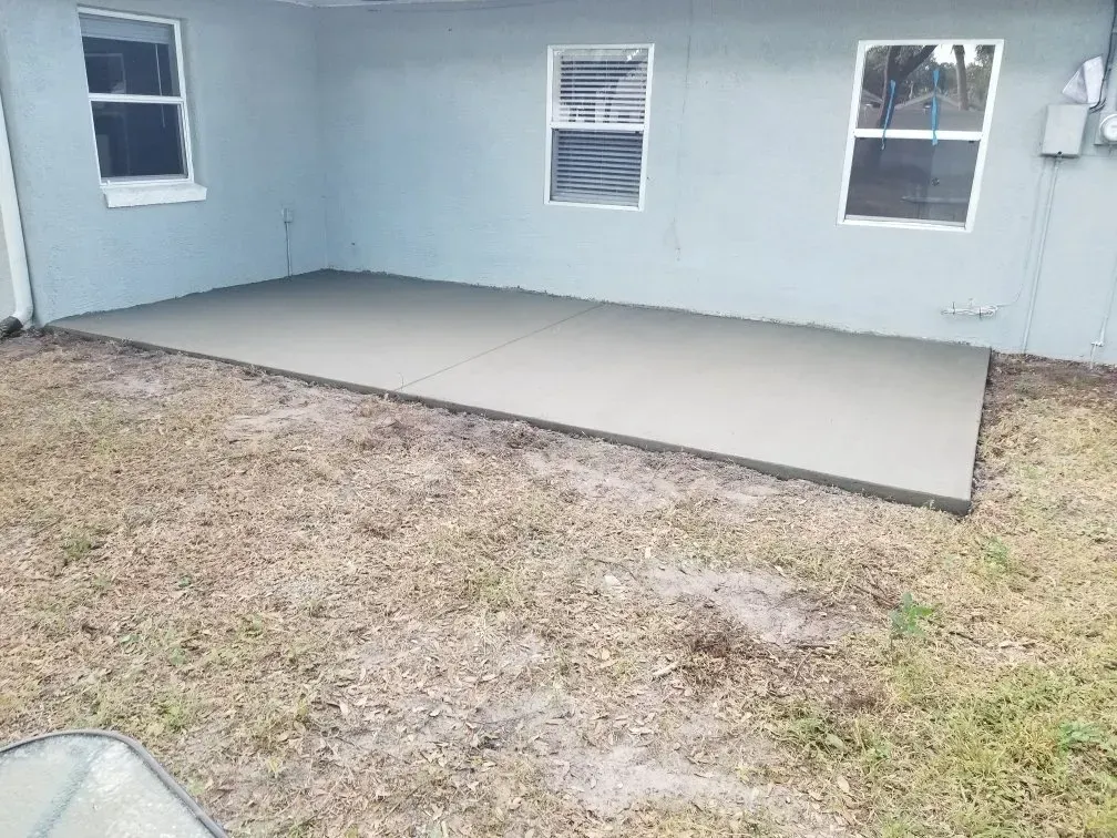 A newly poured concrete patio outside a light blue building, set on dry grass.
