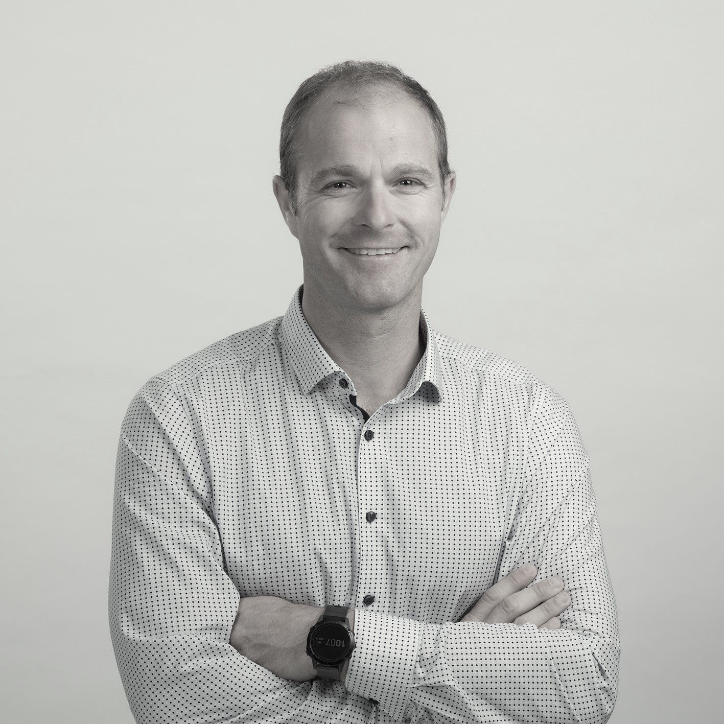 A man in a white shirt is standing with his arms crossed and smiling in a black and white photo.