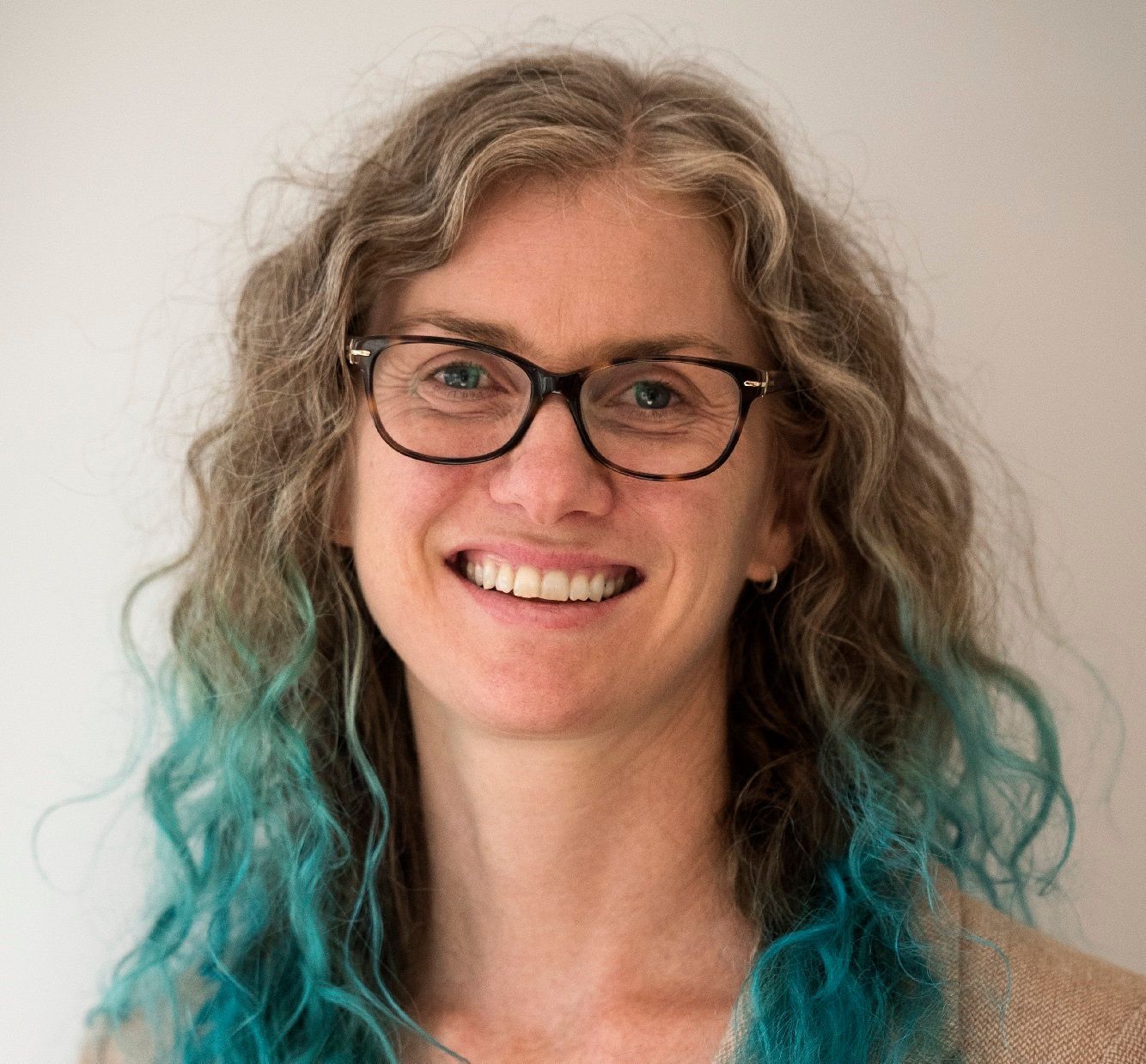 A woman with blue hair and glasses is smiling for the camera.