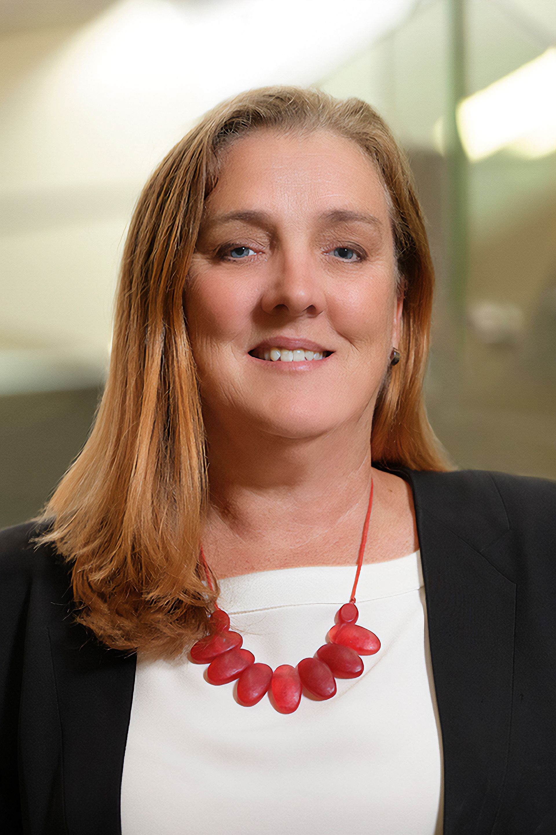 A woman wearing a red necklace and a black jacket is smiling for the camera.