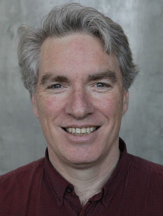 A man with gray hair and a red shirt is smiling for the camera.