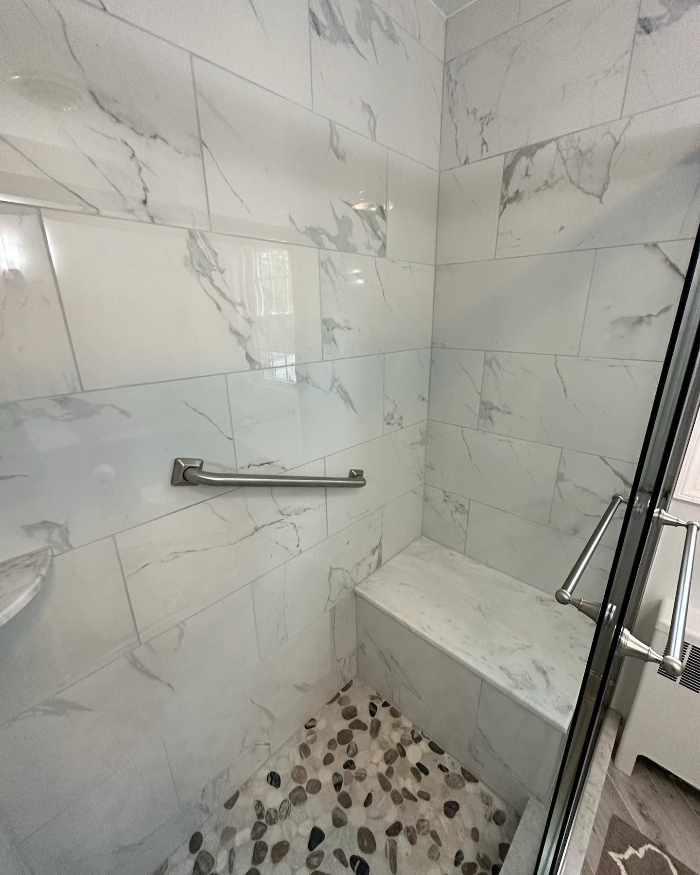 A bathroom with marble tiles and a walk in shower with a bench.