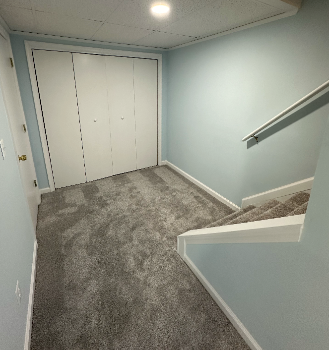 A hallway with stairs leading up to a closet