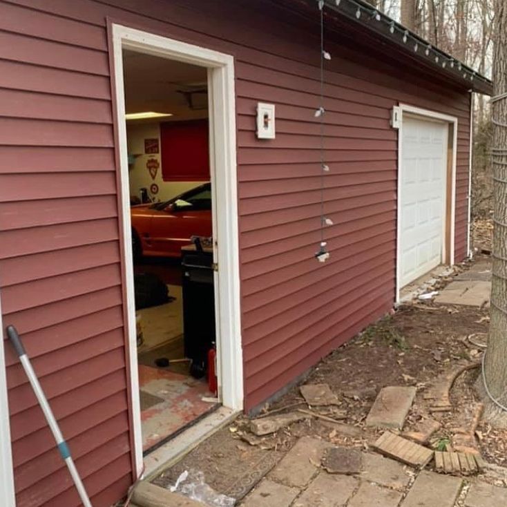 A red garage with the door open and a broom in front of it