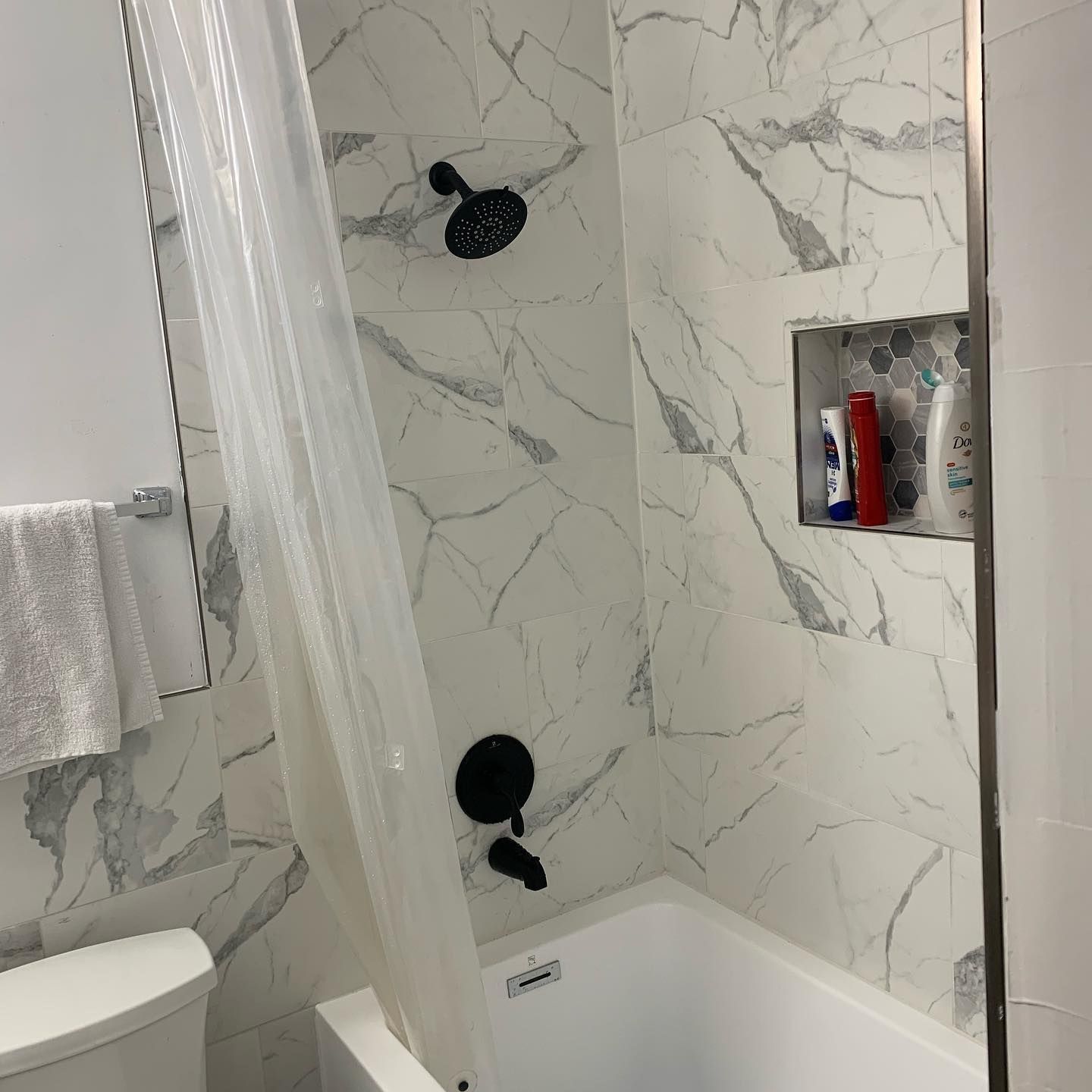 A bathroom with a tub , toilet , shower and marble tiles.