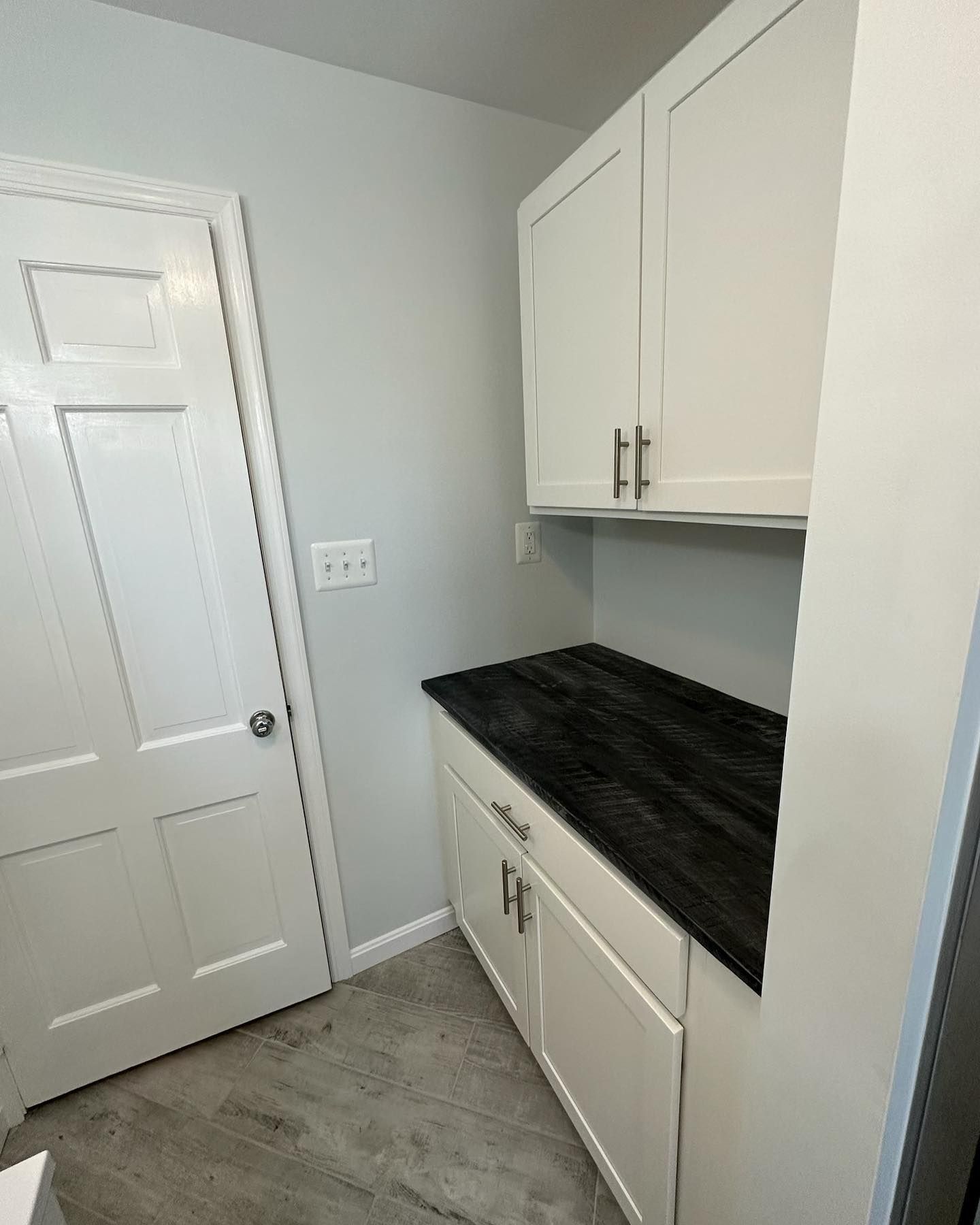A laundry room with white cabinets and a black counter top.
