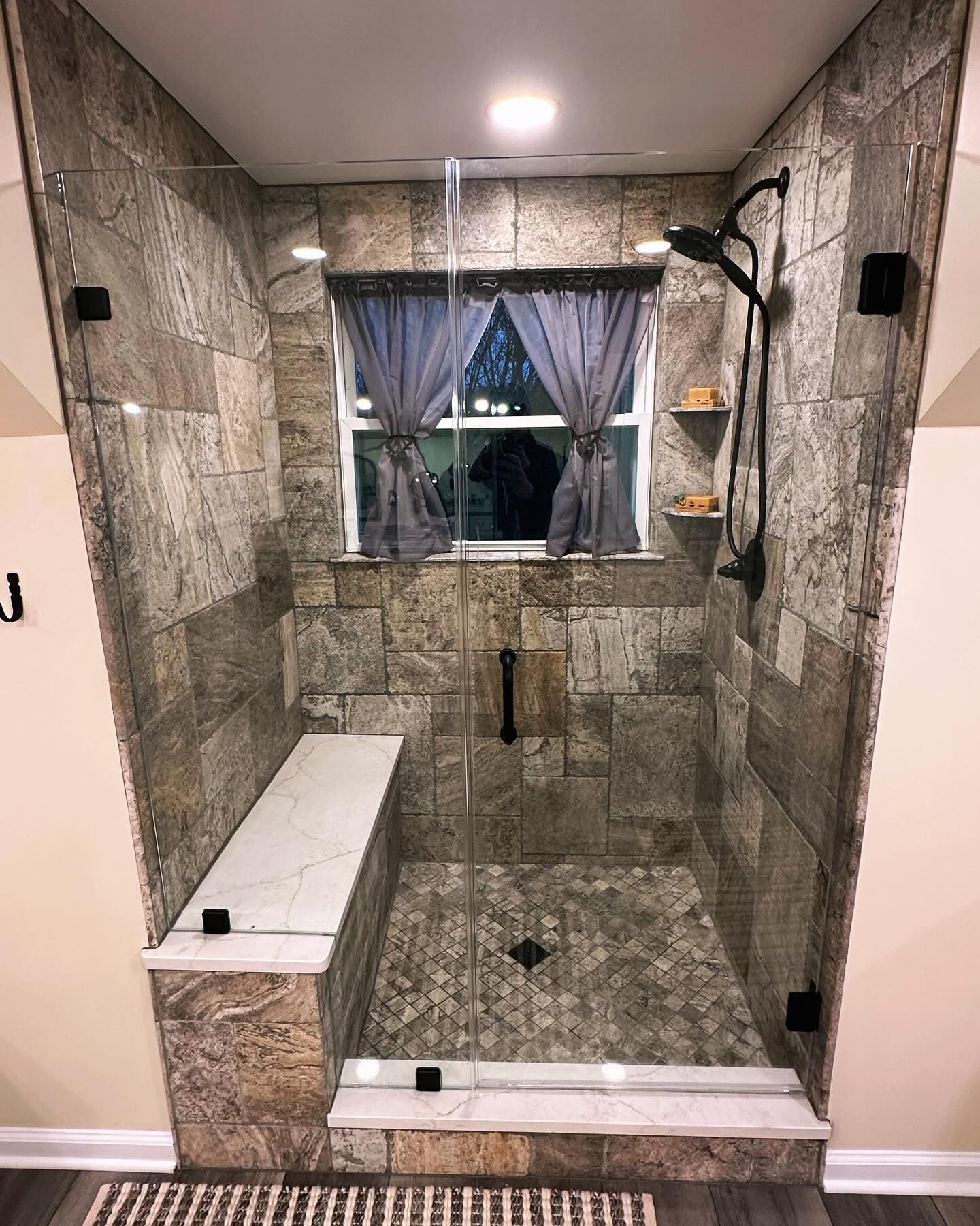 A bathroom with a walk in shower with a bench and a window.