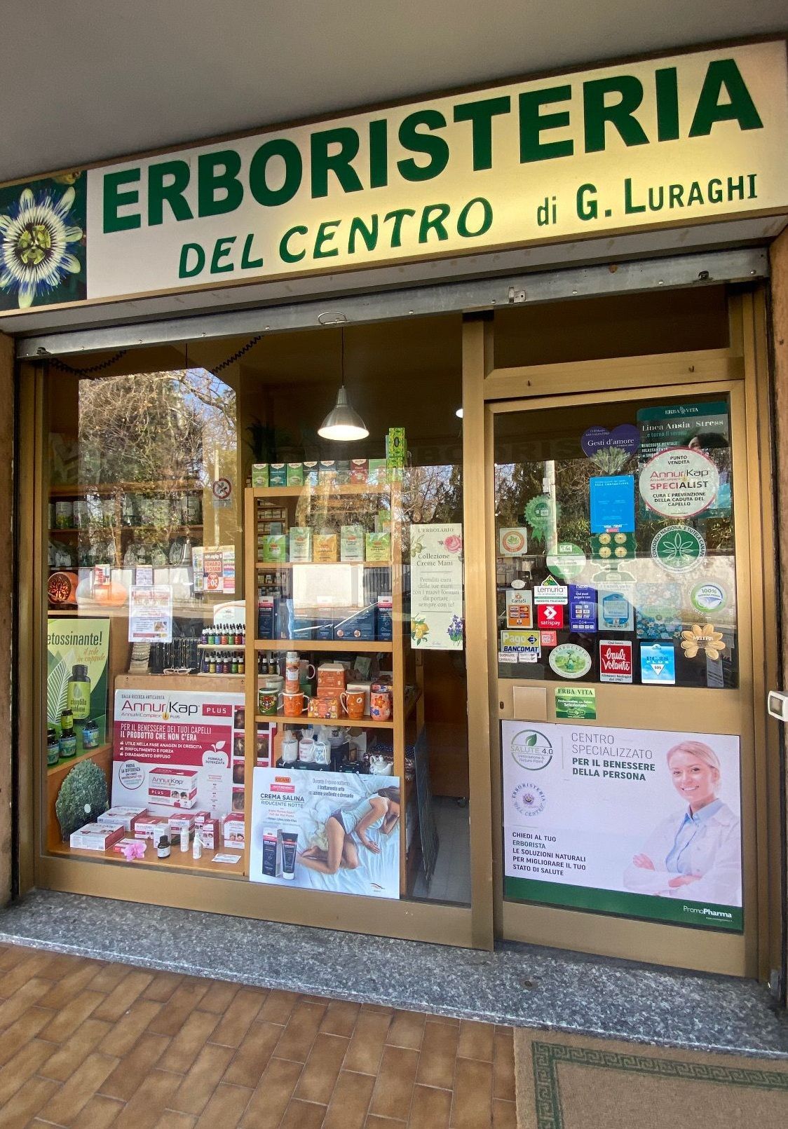 Vetrina di un negozio di erboristeria con insegne verdi, esposizione di prodotti e pubblicità.