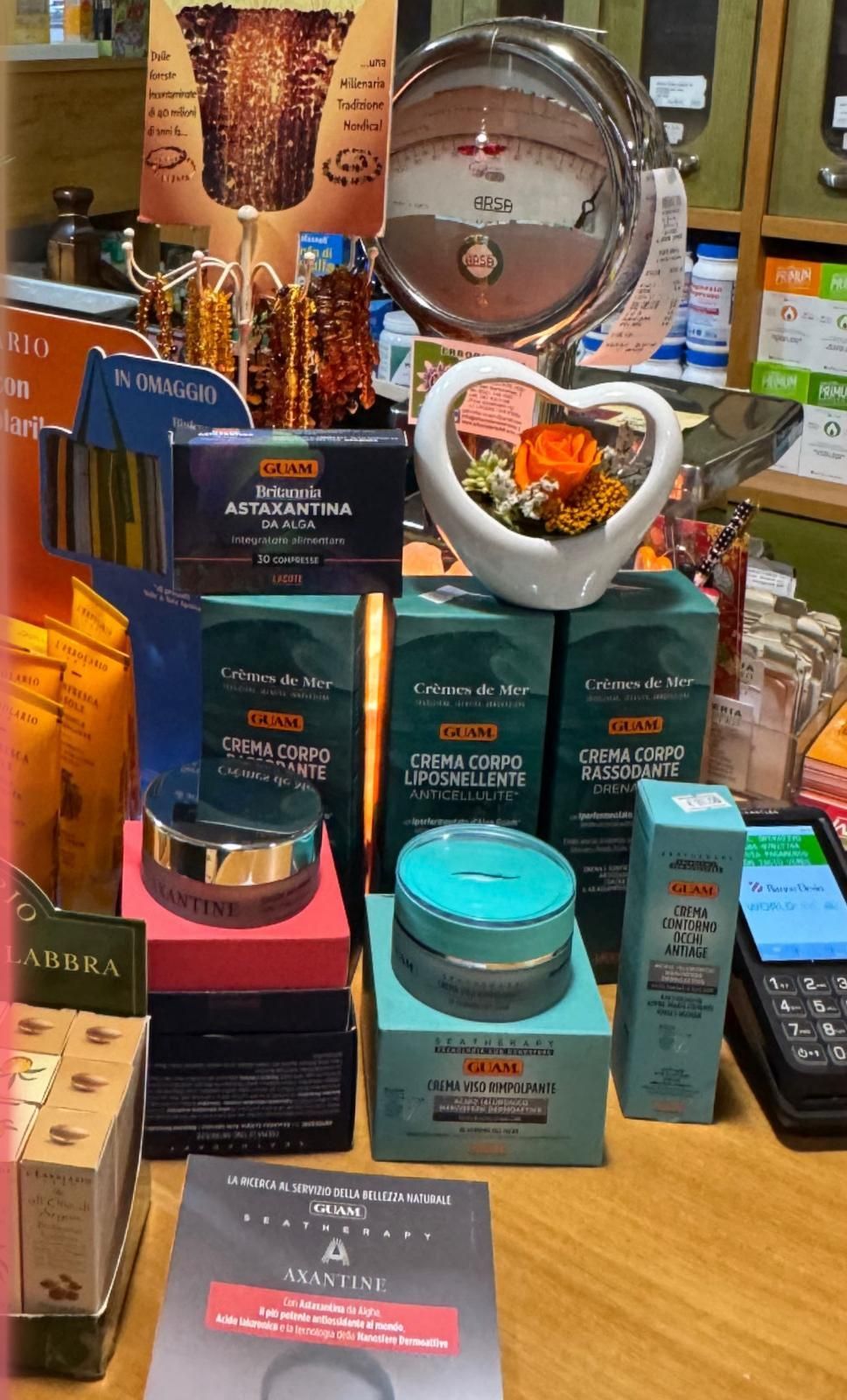 Esposizione di cosmetici su un tavolo di legno con varie scatole, barattoli e un vaso di fiori a forma di cuore.