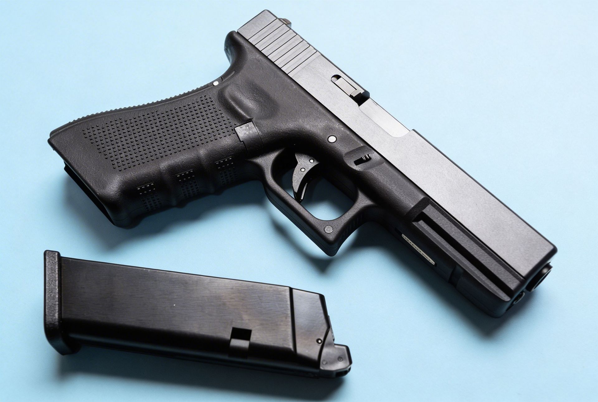 A black semi-automatic pistol resting on a blue surface with its detachable magazine lying beside it.