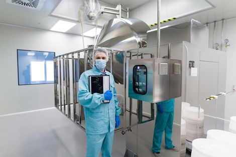 A professional in protective blue gear and a face mask holds a clipboard inside a sterile, high-tech laboratory.