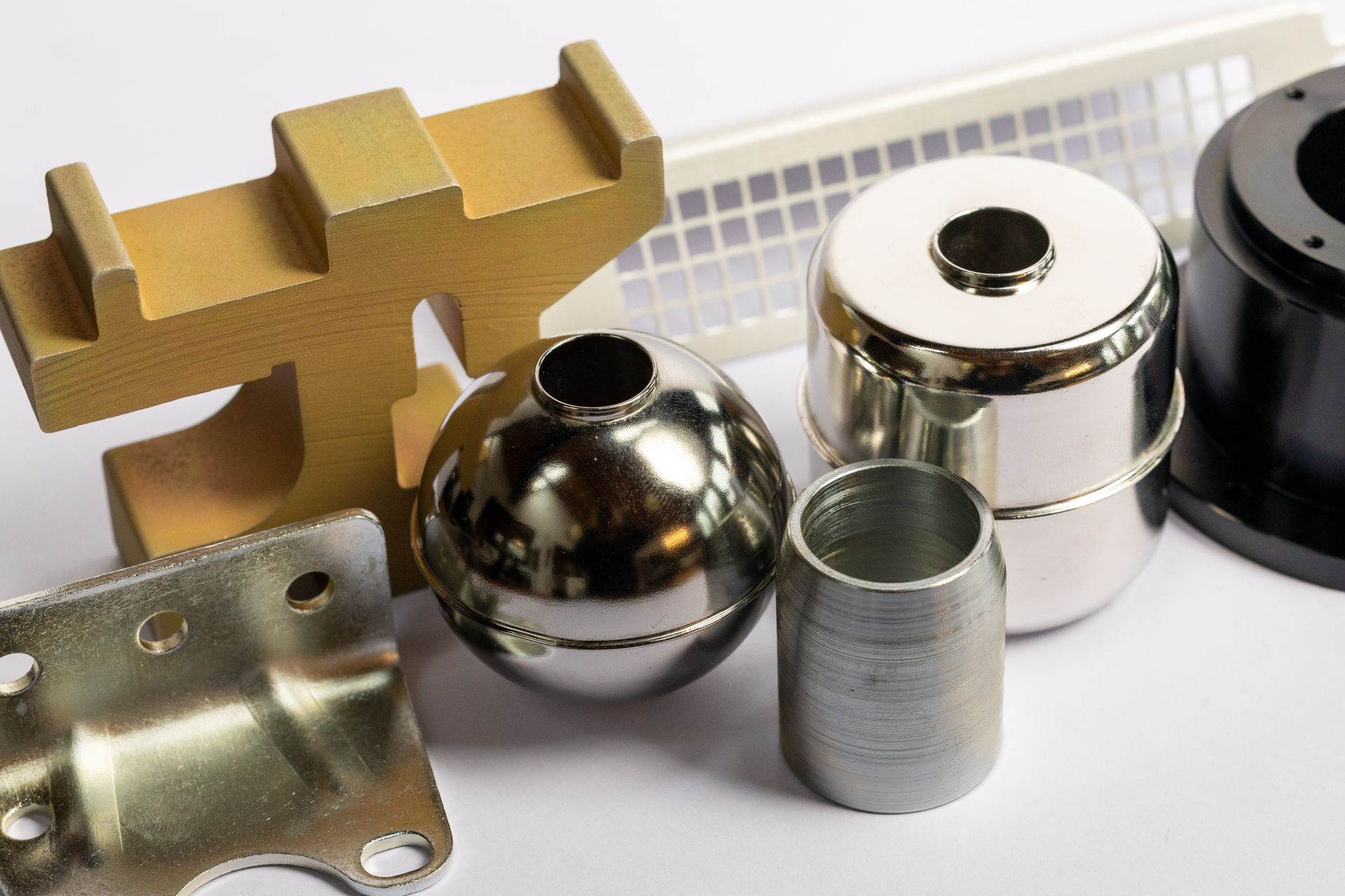 A collection of various industrial metal components and parts, including a gold-colored bracket, sphere, and cylinders.