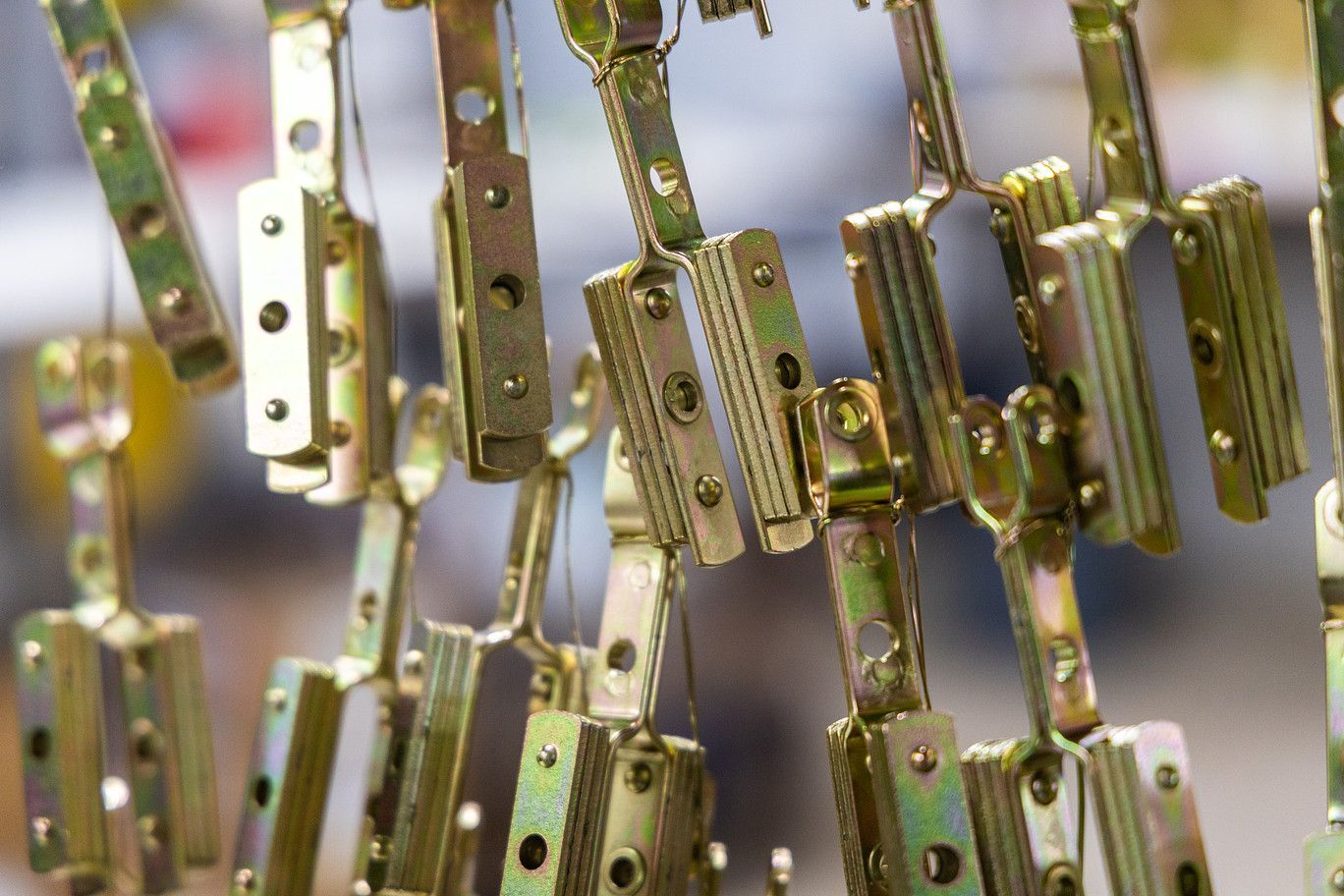Metallic, brass-colored industrial fasteners hang in rows, suspended by hooks in a manufacturing facility.