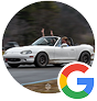 A white Mazda Miata convertible driving on a road with a passenger waving their arms in the air.