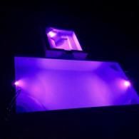 A rectangular swimming pool lit with vibrant purple underwater lights at night, with a small hot tub above it.