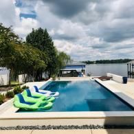An infinity pool overlooking a lake on a cloudy day, with two lime-green inflatable loungers floating in the water.