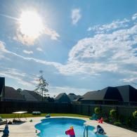 A backyard swimming pool on a sunny day with houses in the background and inflatable toys in the water.
