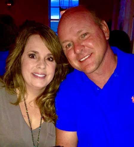 A smiling couple poses for a close-up photo in an indoor setting with blue lighting visible in the background.